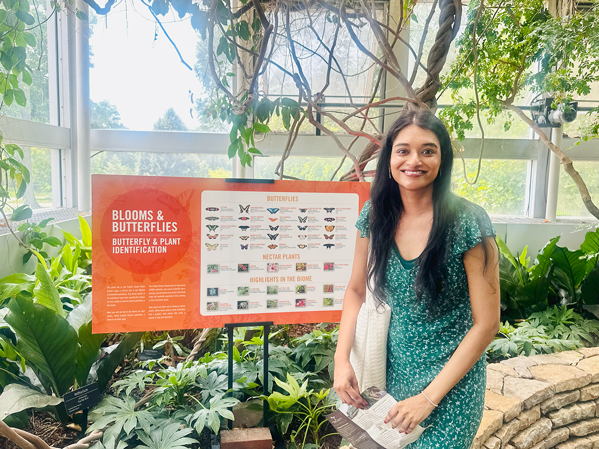 Dr. Bindu Challa poses next to the Butterfly and Plant Identification Guide in the Franklin Park Conservatory & Botanical Gardens