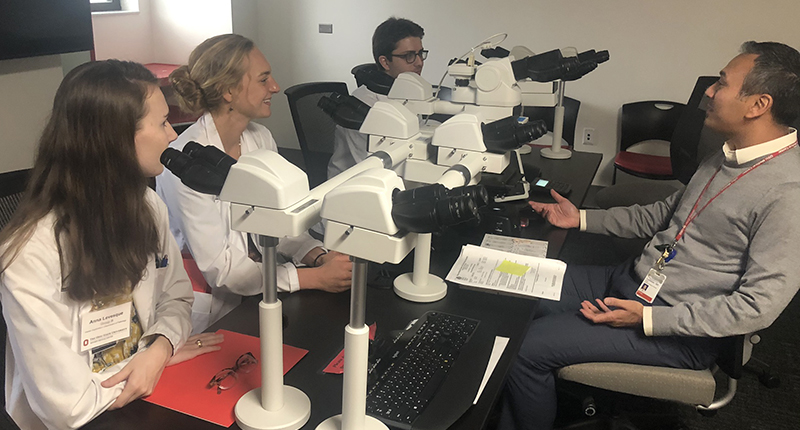 Three medical students and Dr. Gary Tozbikian are seated around a multi-headed microscope. They are engaged in a discussion.