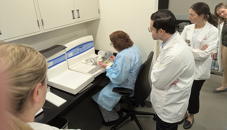 A small group of medical students are looking over the Renal Histology Lab Managers shoulder as she fixes tissue in wax so it can be cut in slides.