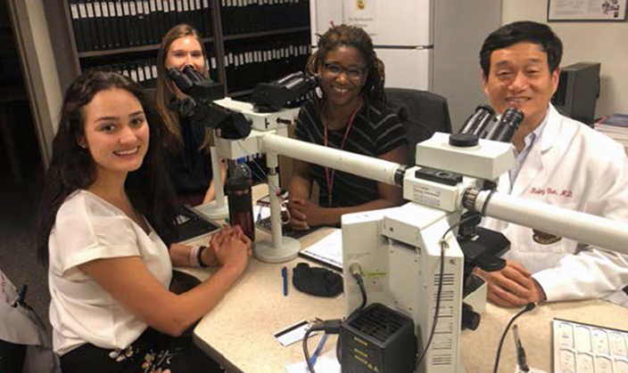 Two Medical students are seated at a multi-headed mircroscope with Drs. I-Sanna Gibbons-Fideler and Rulong Shen in the Cytology lab.