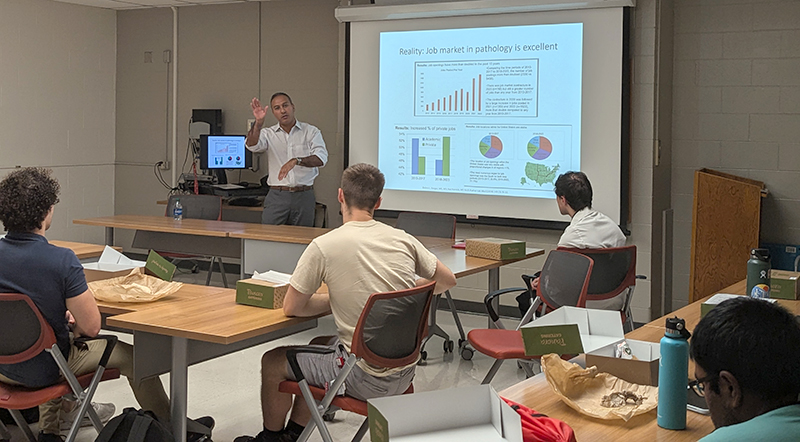 Dr. Gary Tozbikian waves to the camera while giving a presentation to a group of medical students.