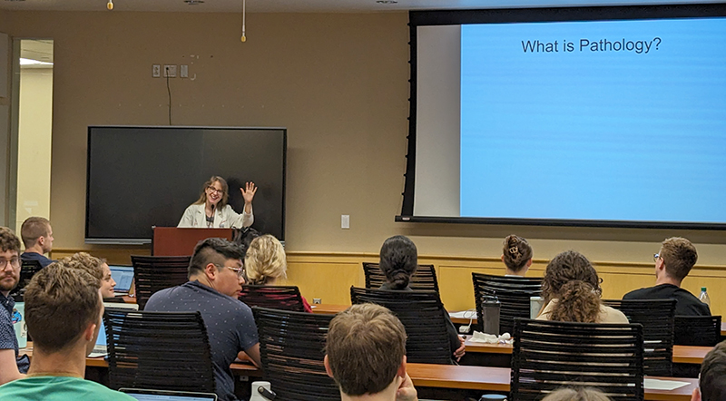 Dr. Debra Zynger waves to the camera while giving a presentation to a group of medical students.